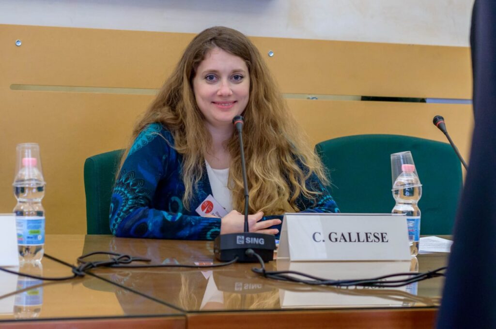 A blonde woman sitting at a conference table smiling